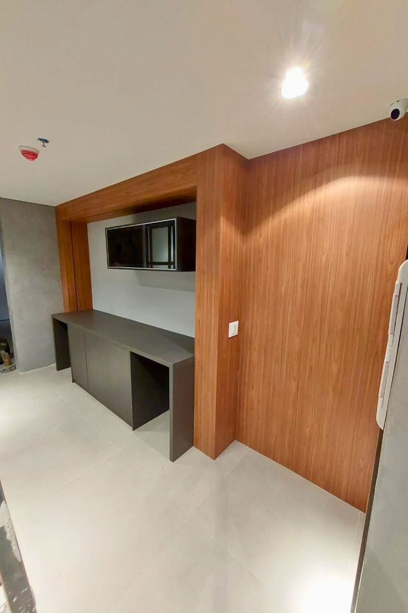 Bar ou cantinho do café planejado em nicho de madeira, com balcão cinza escuro e armário aéreo com porta de vidro.