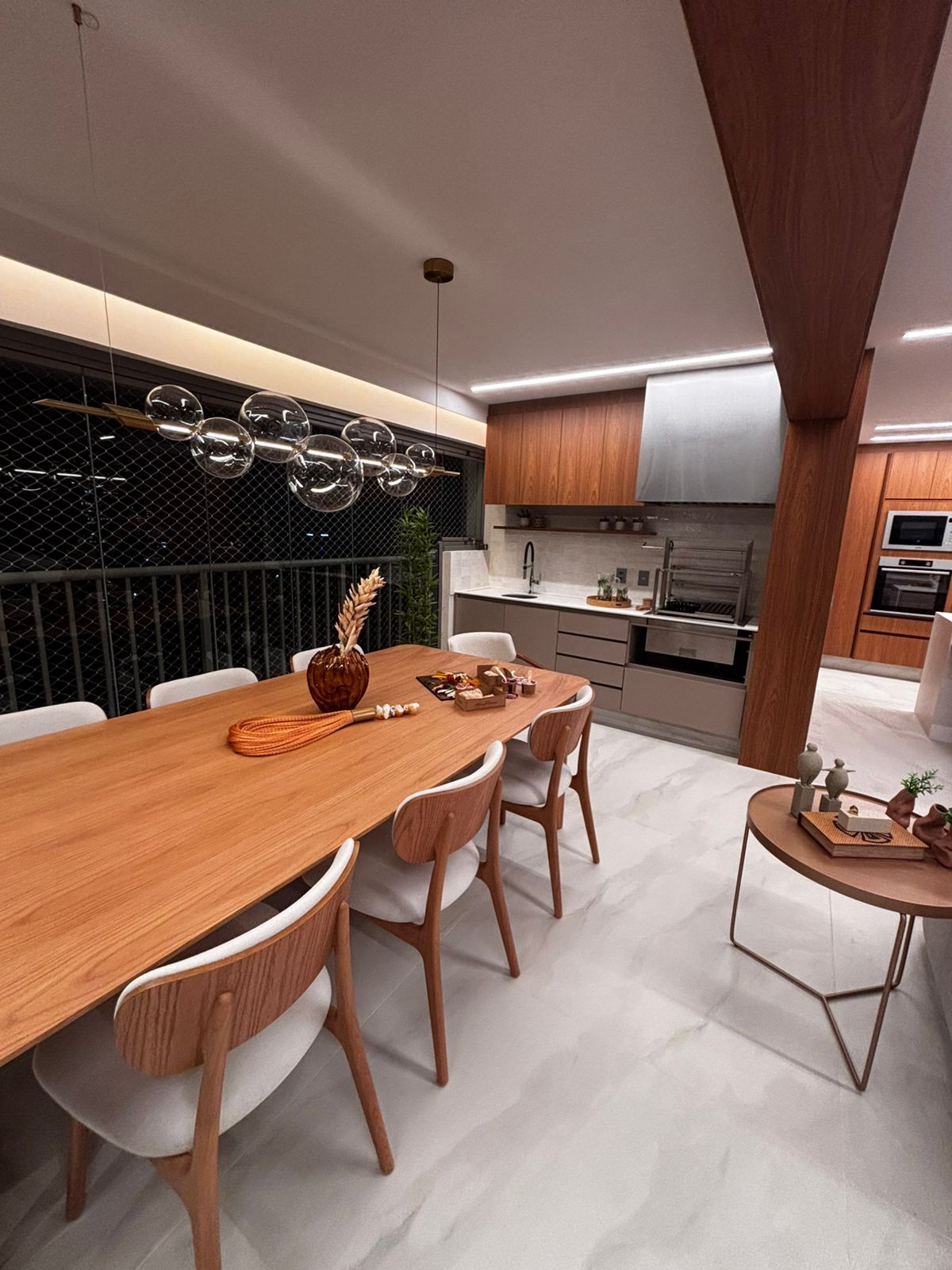 Varanda gourmet planejada em apartamento com churrasqueira, armários brancos sob medida e revestimento de parede em madeira.