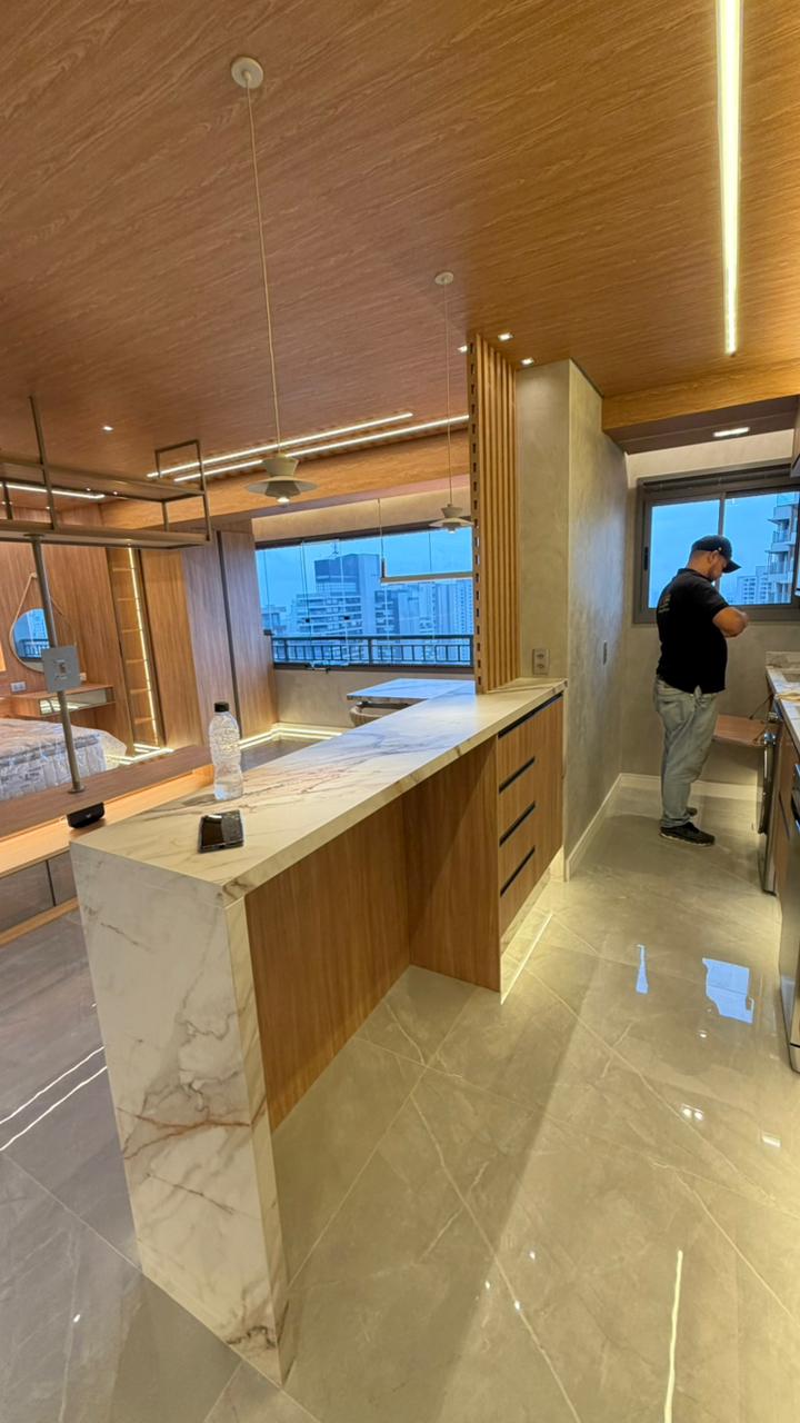 Bar ou cantinho do café planejado em nicho de madeira, com balcão cinza escuro e armário aéreo com porta de vidro.