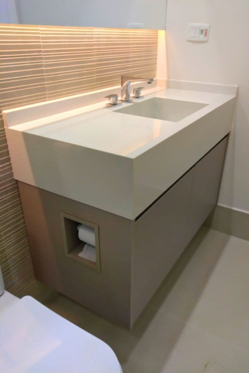 Detalhe de gabinete de banheiro planejado em tom fendi (cinza quente) com bancada de pedra branca e cuba esculpida.