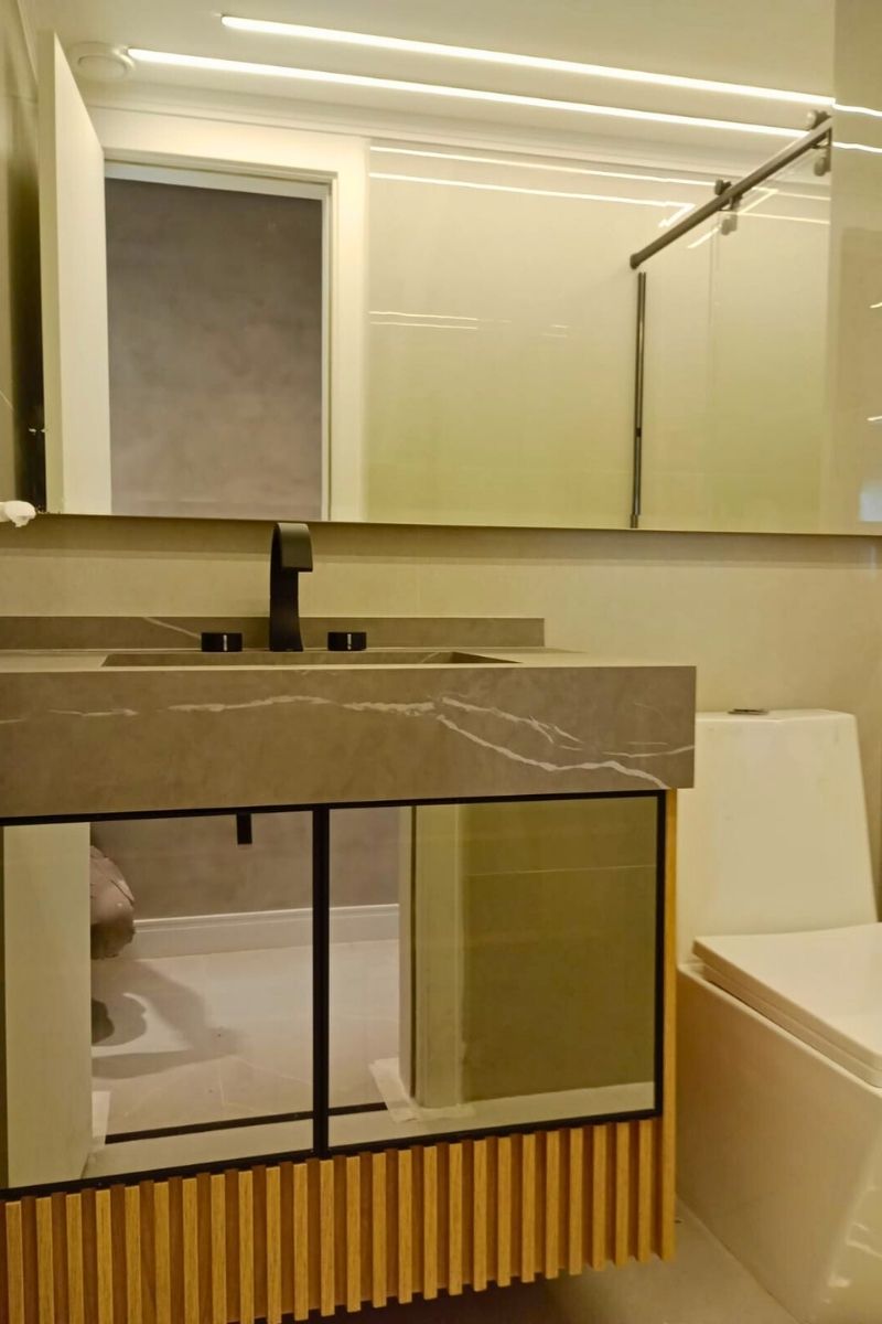 Detalhe de bancada de lavabo com cuba esculpida em porcelanato marmorizado e torneira de mesa preta fosca.