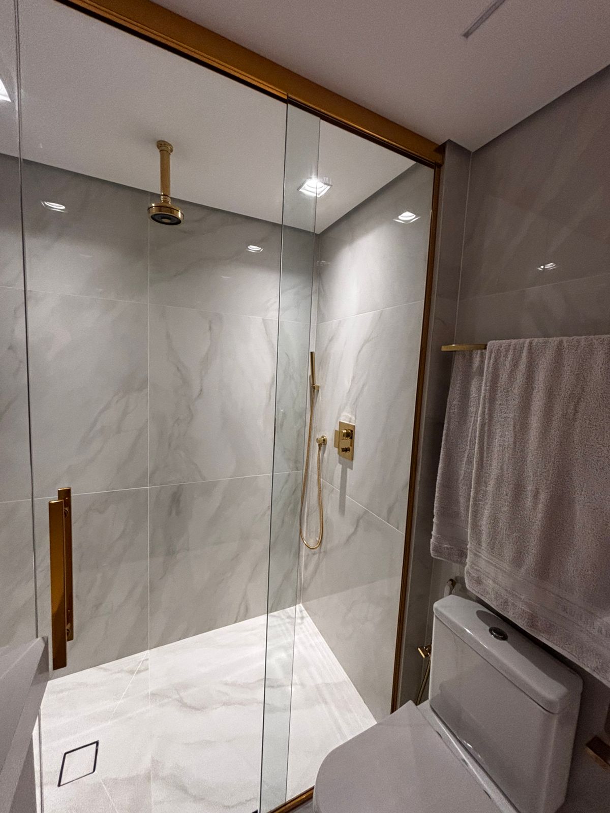 Banheiro planejado moderno com nichos de madeira sobre a caixa acoplada, espelho com iluminação LED e revestimento escuro.