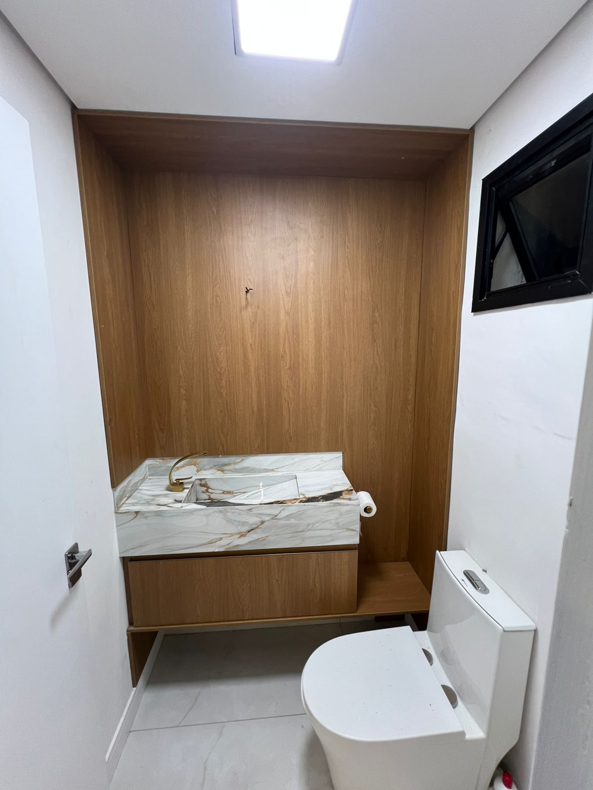 Detalhe de gabinete de banheiro planejado em tom fendi (cinza quente) com bancada de pedra branca e cuba esculpida.