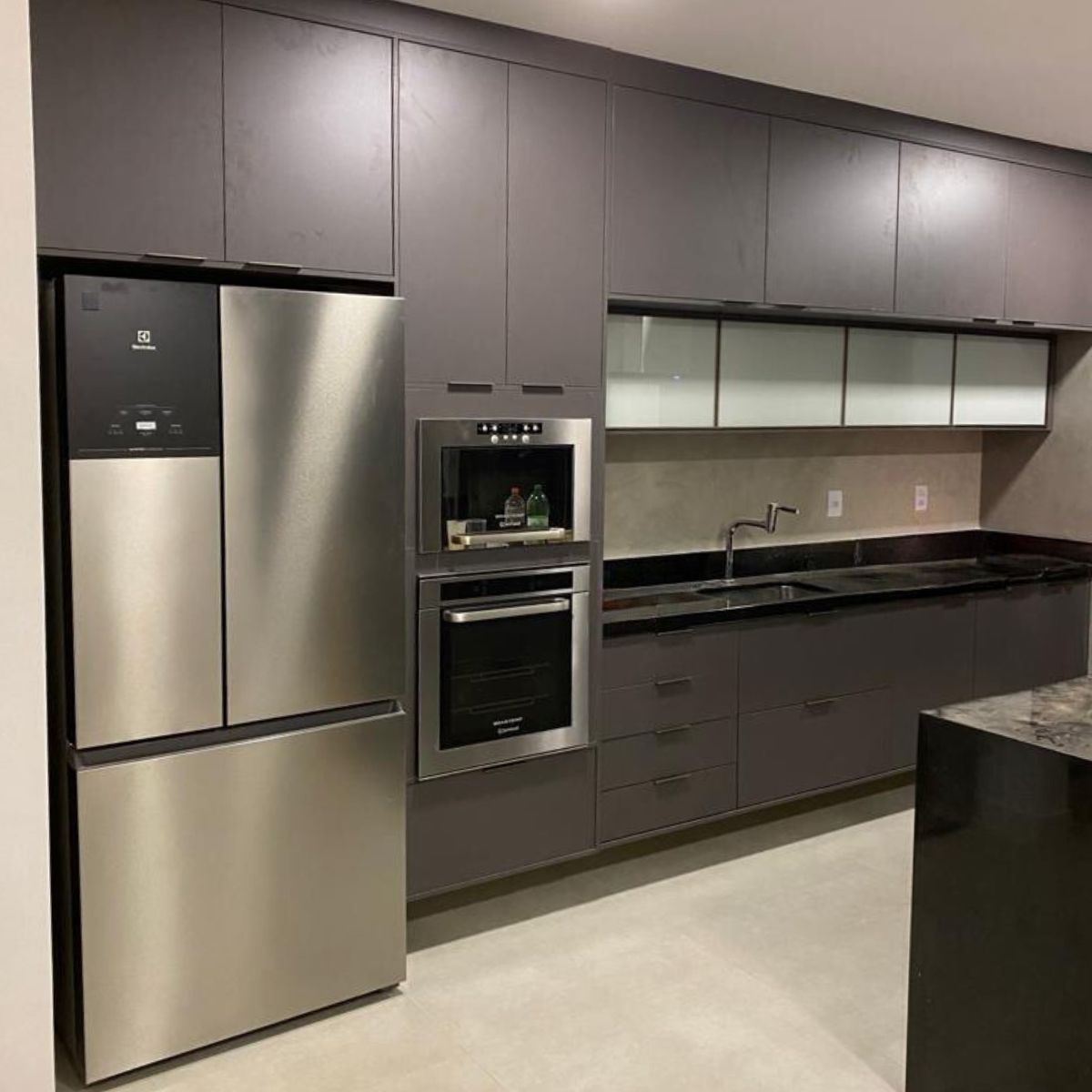 Cozinha planejada sofisticada em cinza chumbo, com torre quente para forno embutido e nicho para geladeira side-by-side.