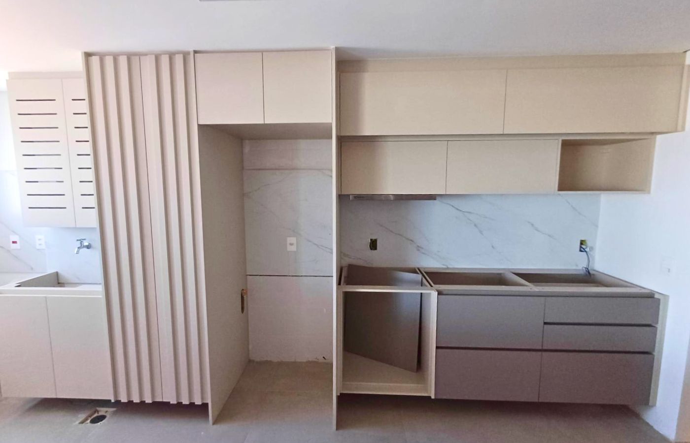 Cozinha planejada em L na cor branca sendo finalizada, com detalhe lateral em marcenaria ripada vertical.