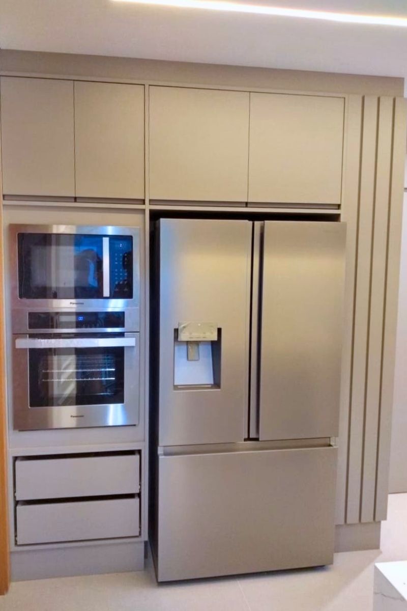 Nicho planejado sob medida para geladeira side-by-side em aço inox, integrado a uma torre de fornos embutida.