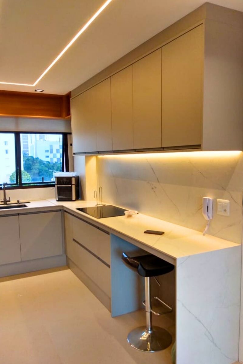 Cozinha sob medida em apartamento, com armários em tom neutro, cooktop de indução e revestimento de parede marmorizado.