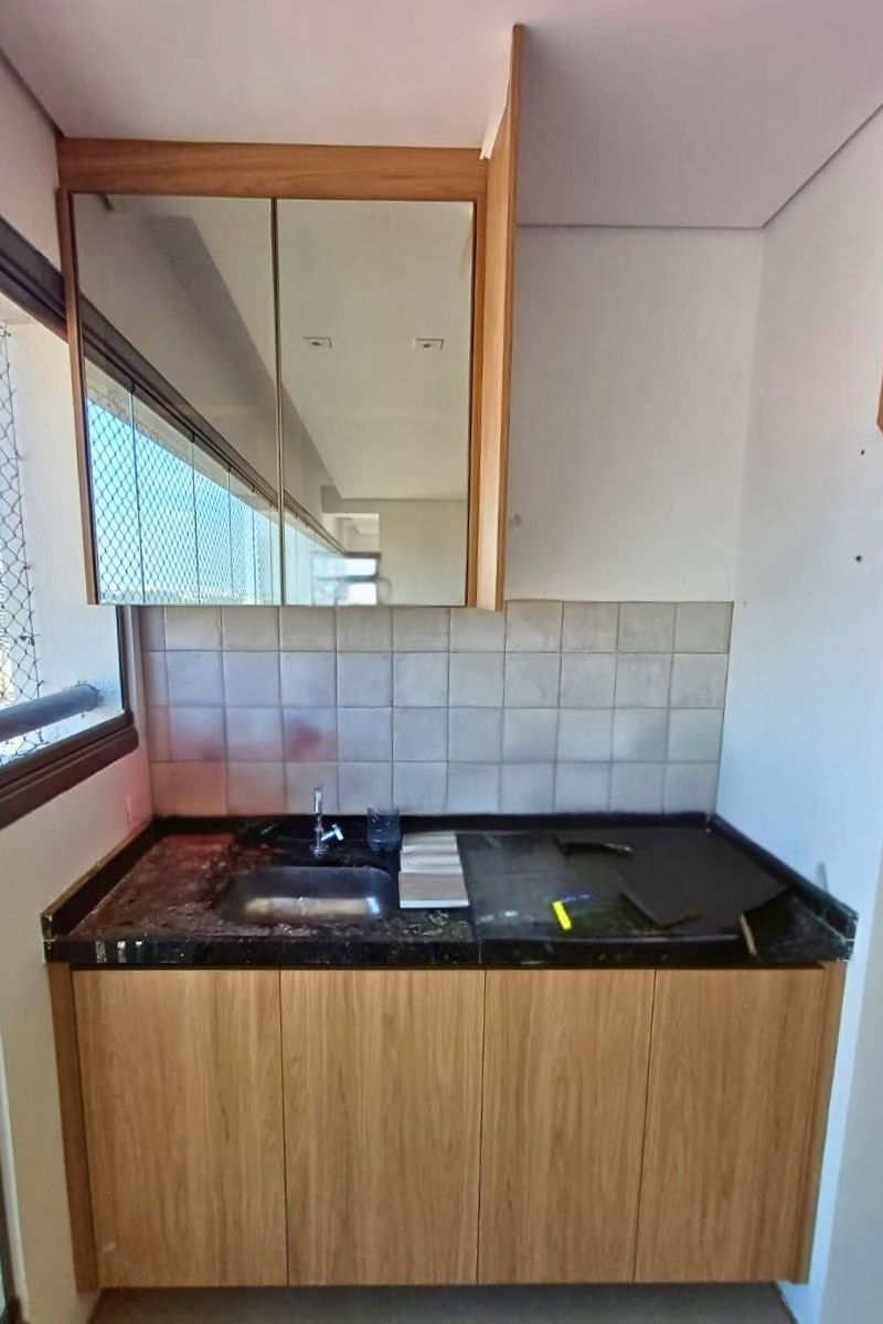 Cozinha compacta de apartamento na Zona Leste com armários aéreos espelhados e bancada em granito preto.