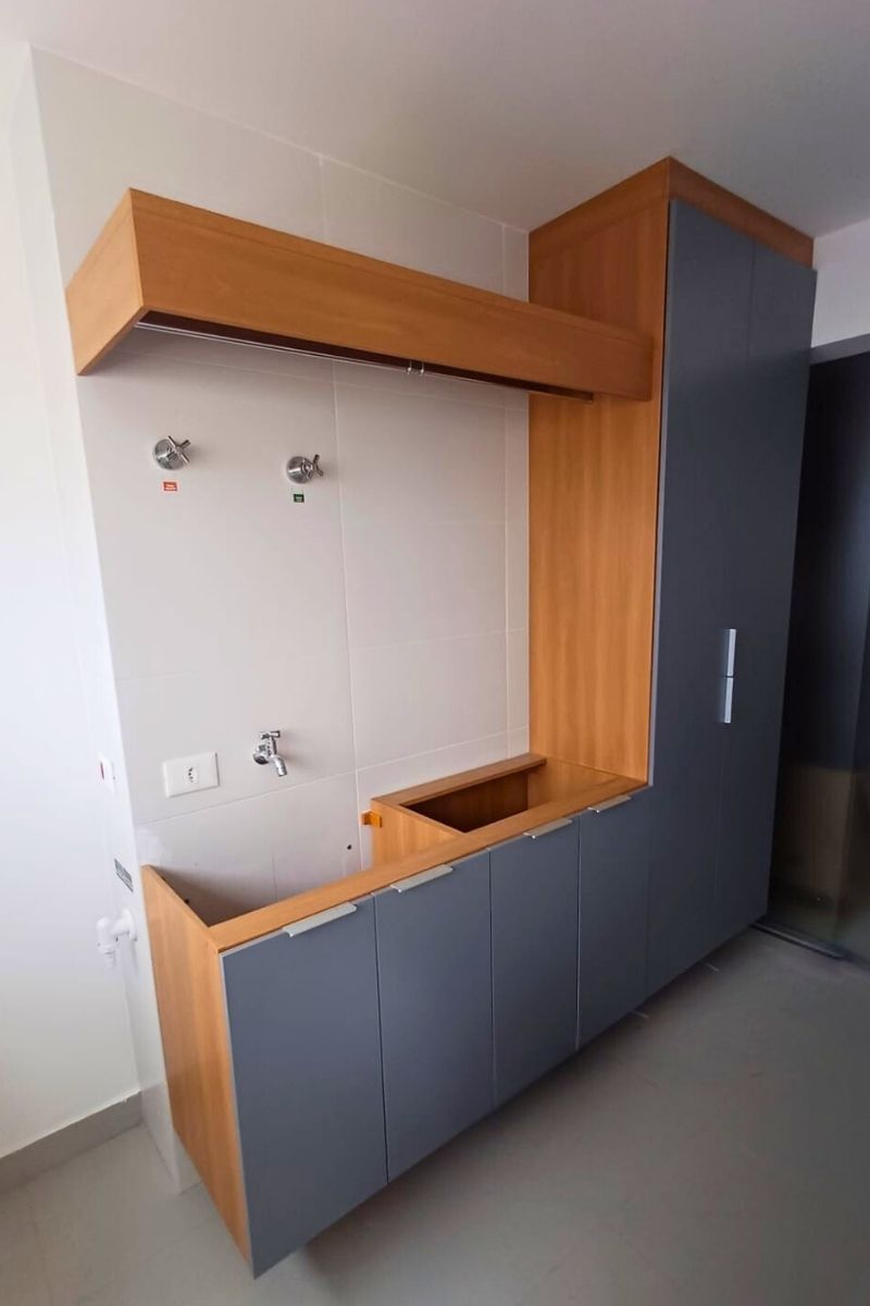 Área de serviço planejada com armários brancos discretos, nicho decorativo amadeirado e revestimento clean.