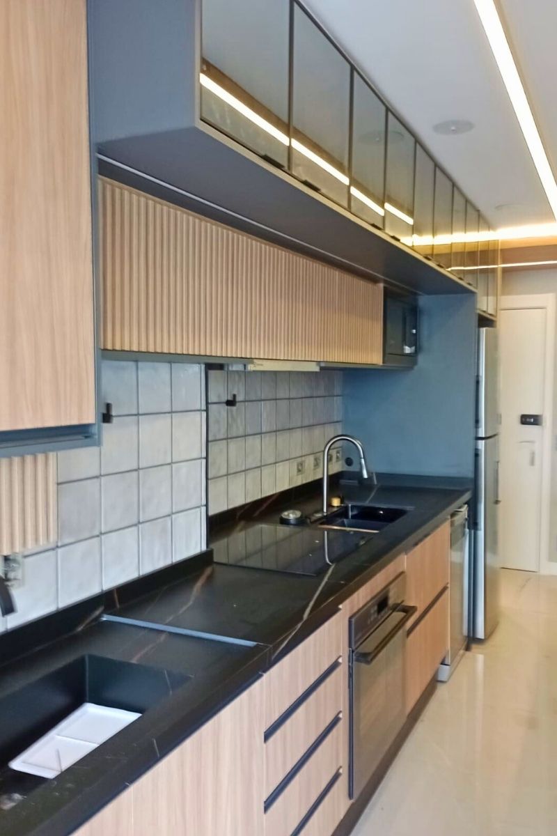 Bancada de pia de cozinha planejada com granito preto absoluto, torneira gourmet moderna e armários inferiores com detalhe ripado em madeira.