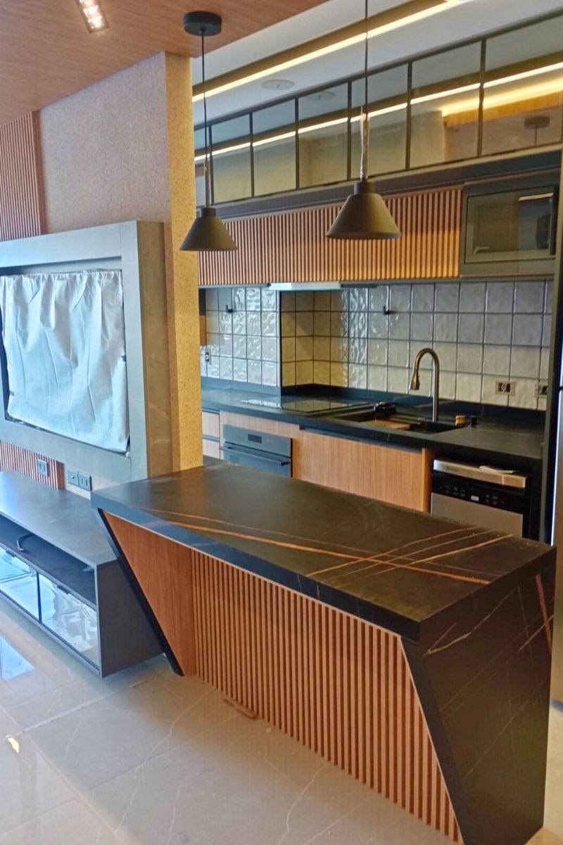 Cozinha americana com península (balcão) em pedra preta e marcenaria planejada combinando madeira e tons de cinza, integrando os ambientes.