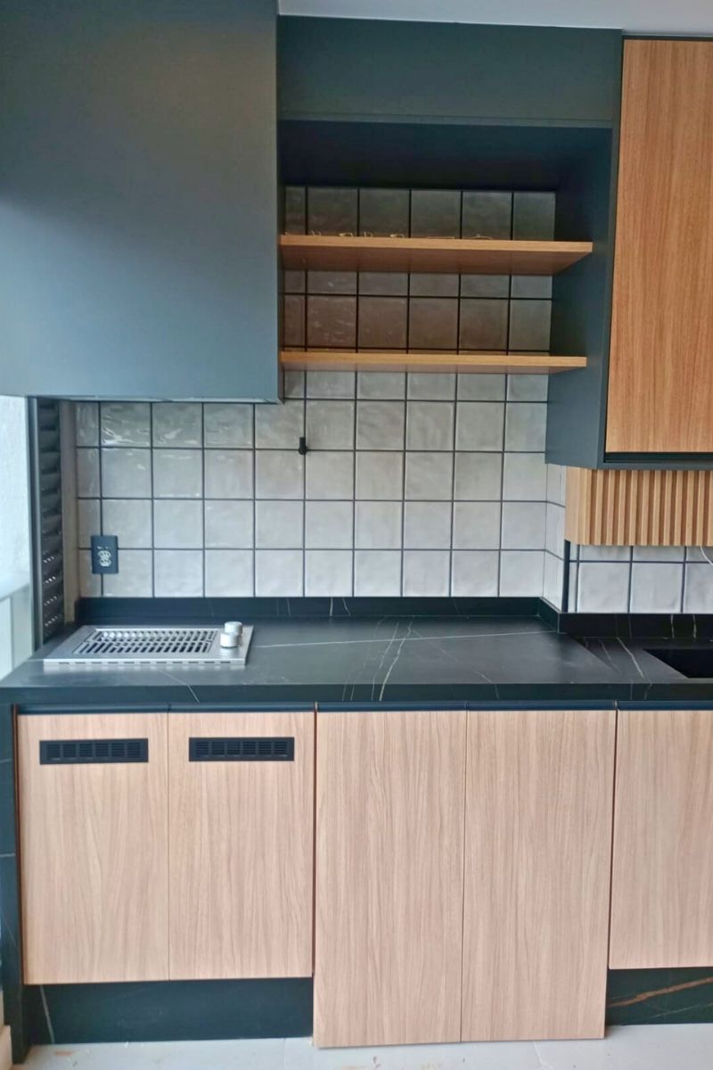 Detalhe do revestimento de parede (backsplash) com azulejos brancos quadrados e rejunte escuro, contrastando com a bancada preta e armários aéreos.
