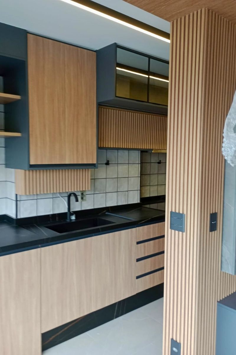 Marcenaria de alto padrão com acabamento ripado vertical em madeira revestindo armários aéreos e colunas estruturais da cozinha.