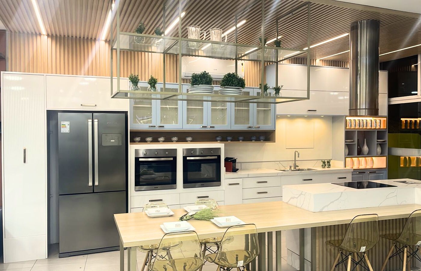 Cozinha gourmet planejada de alto padrão com ilha central, armários brancos e estrutura metálica suspensa (estilo industrial).