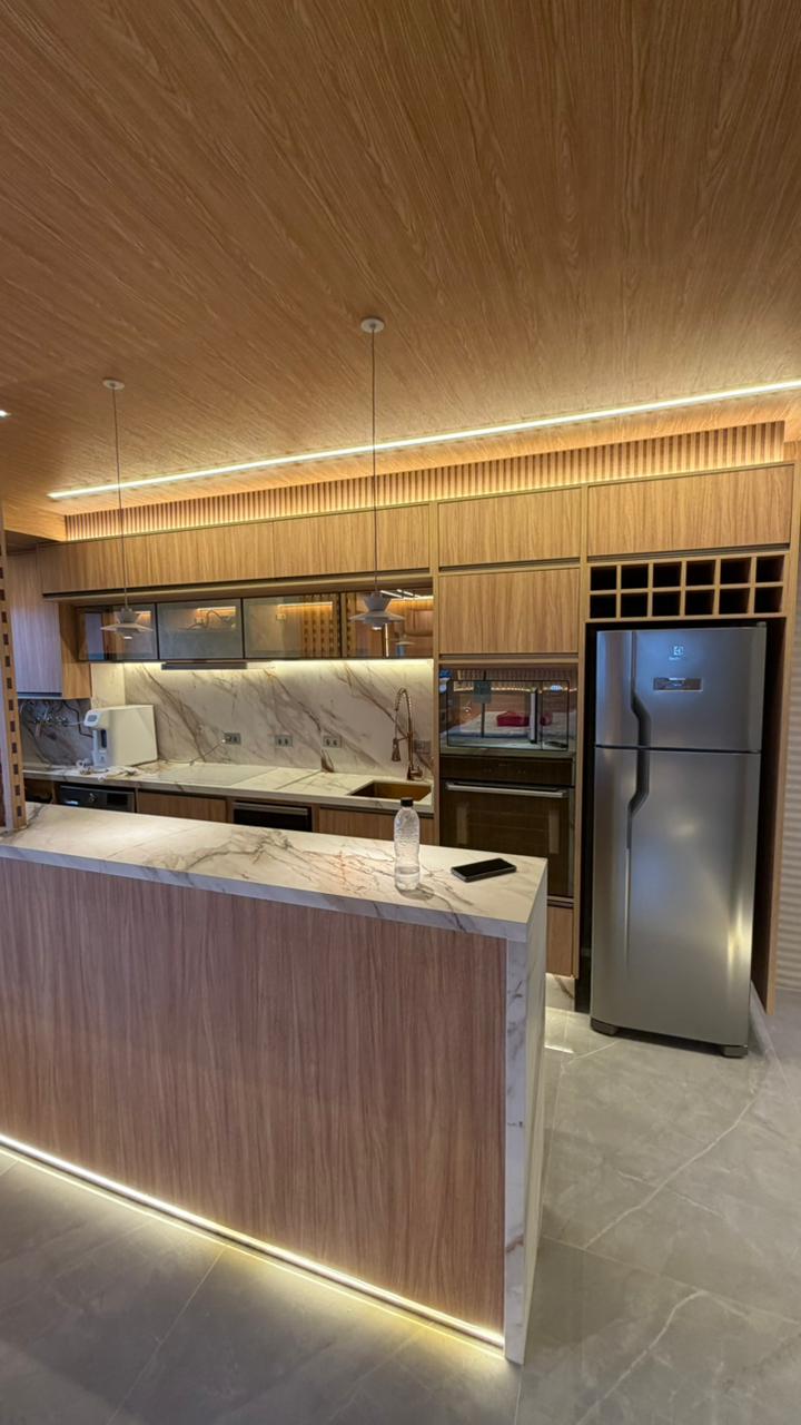 Cozinha gourmet planejada de alto padrão com ilha central, armários brancos e estrutura metálica suspensa (estilo industrial).