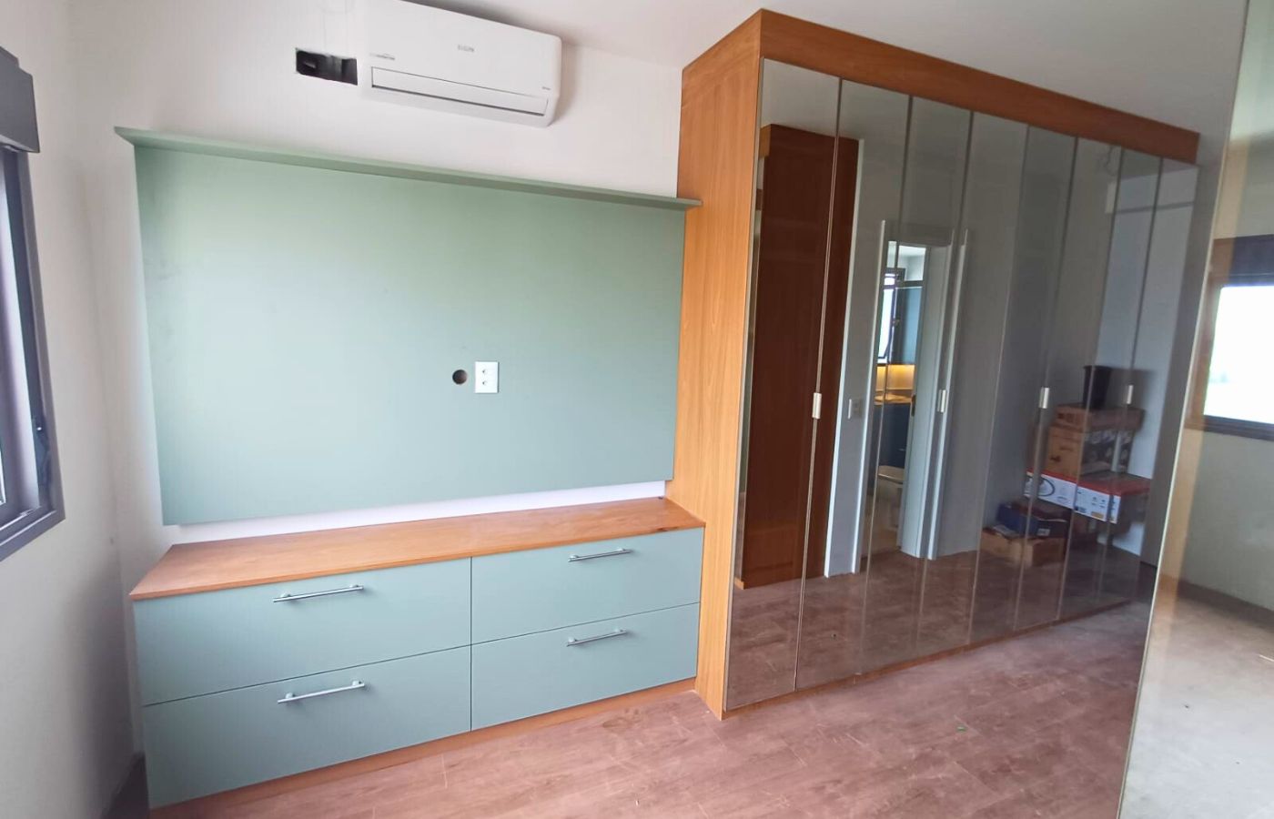 Projeto de dormitório com móvel para TV em tom verde menta, gavetões espaçosos e guarda-roupa com portas espelhadas bronze.