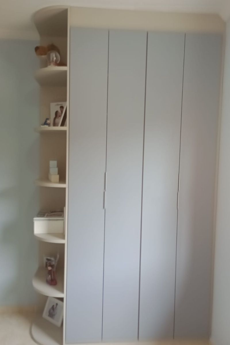 Guarda-roupa planejado branco com puxadores verticais modernos e prateleiras laterais arredondadas (cantoneira) para otimização de espaço.