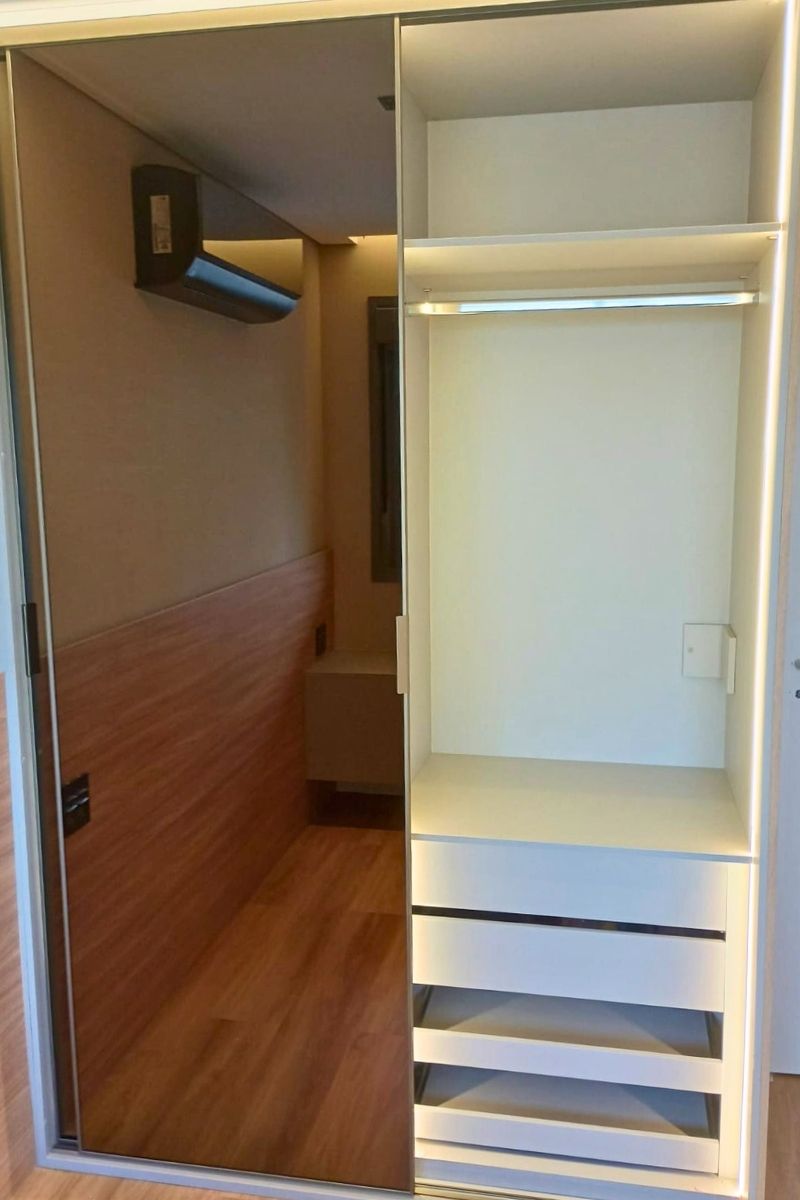 Detalhe de instalação de marcenaria sob medida, mostrando o acabamento entre painéis de madeira e móveis brancos.