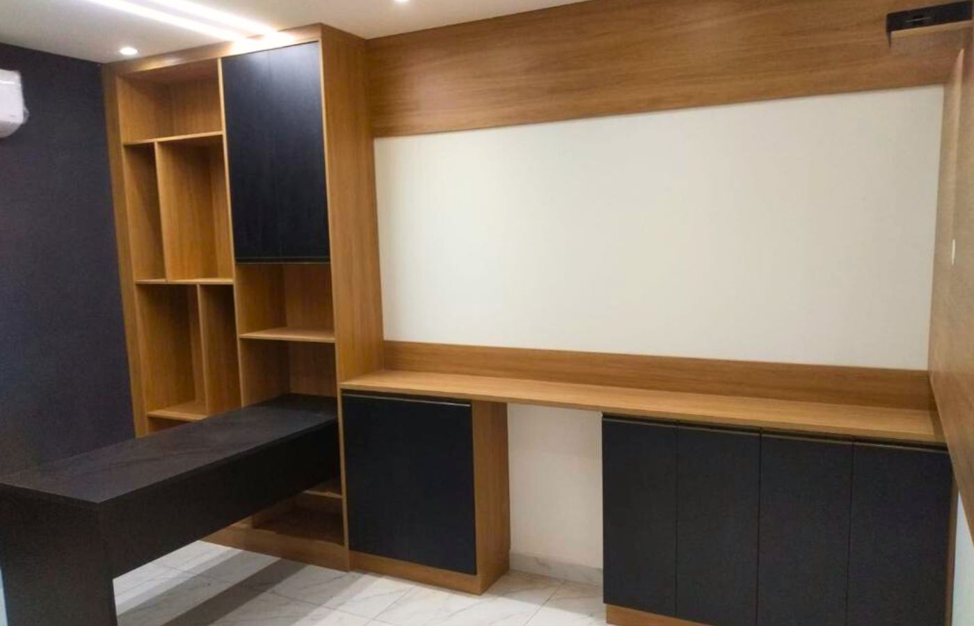 Bancada de trabalho sob medida integrada a armários aéreos pretos e painel de fundo em madeira clara.