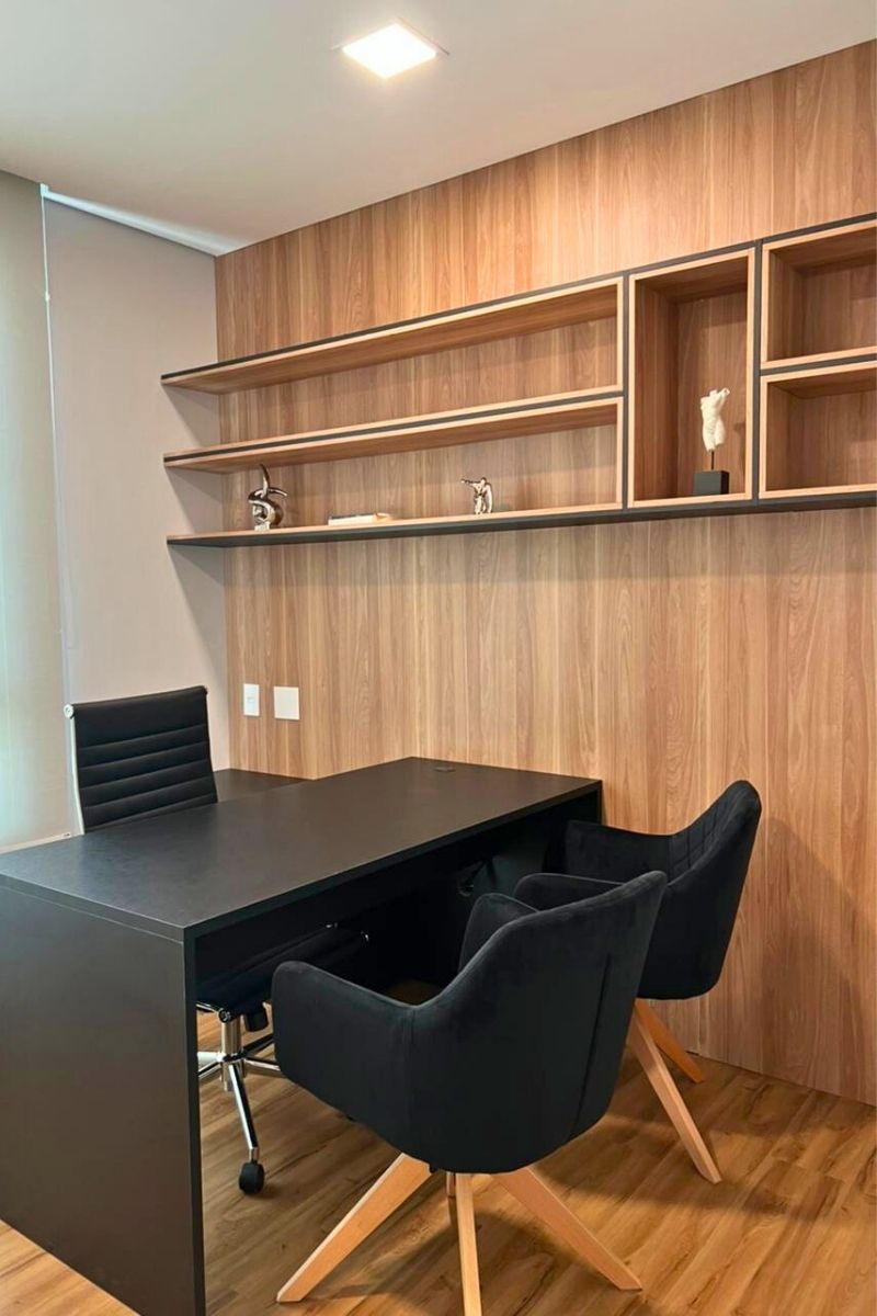 Escritório planejado confortável com mesa preta espaçosa, cadeiras estofadas e prateleiras superiores em madeira.