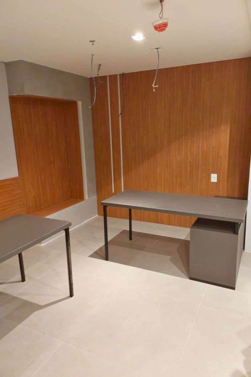 Layout de escritório com mesas de trabalho operacionais cinzas e revestimento de parede em painéis de madeira.