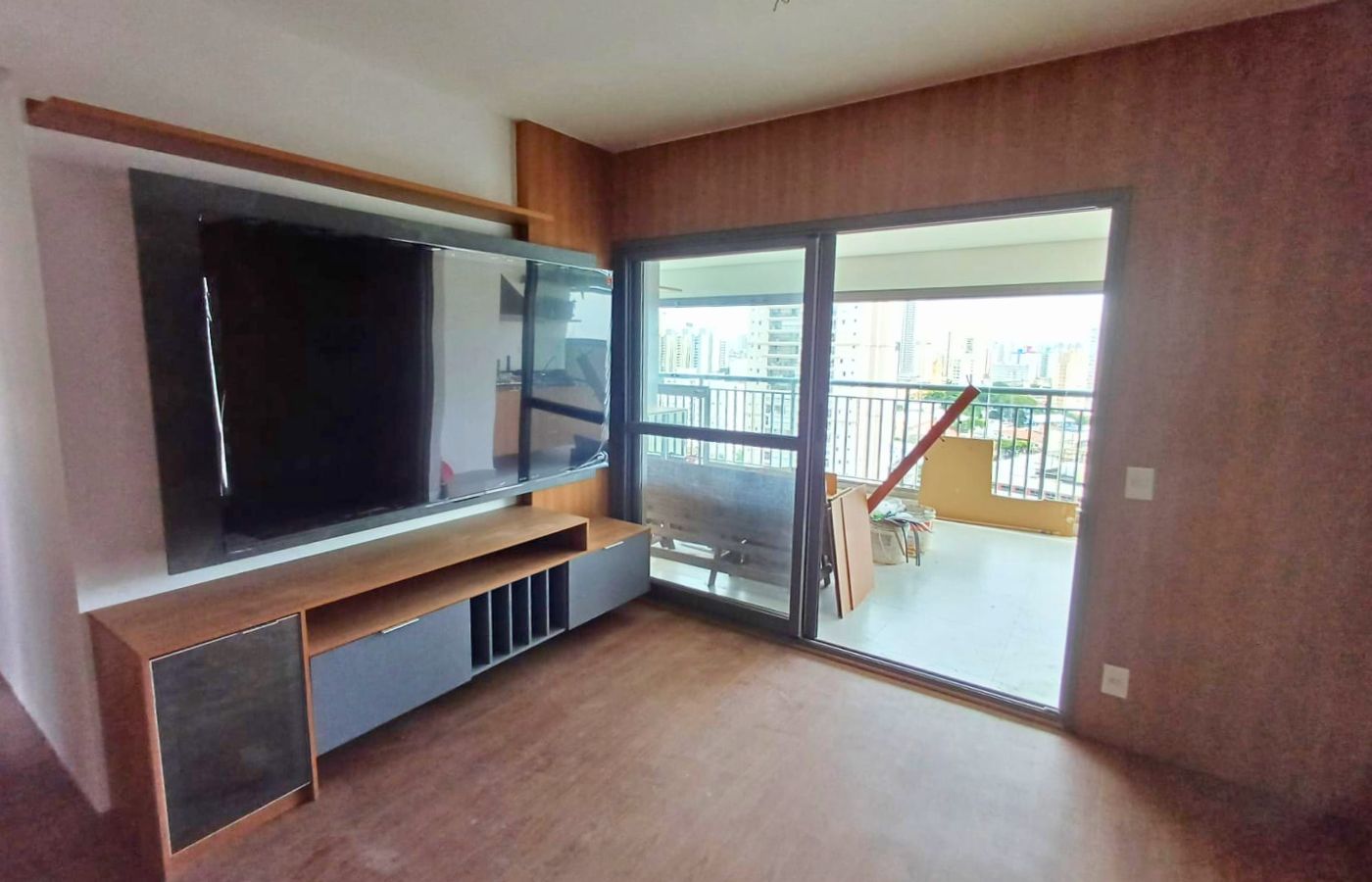 Sala de estar ampla com home theater planejado, rack baixo alongado e integração com a varanda do apartamento.