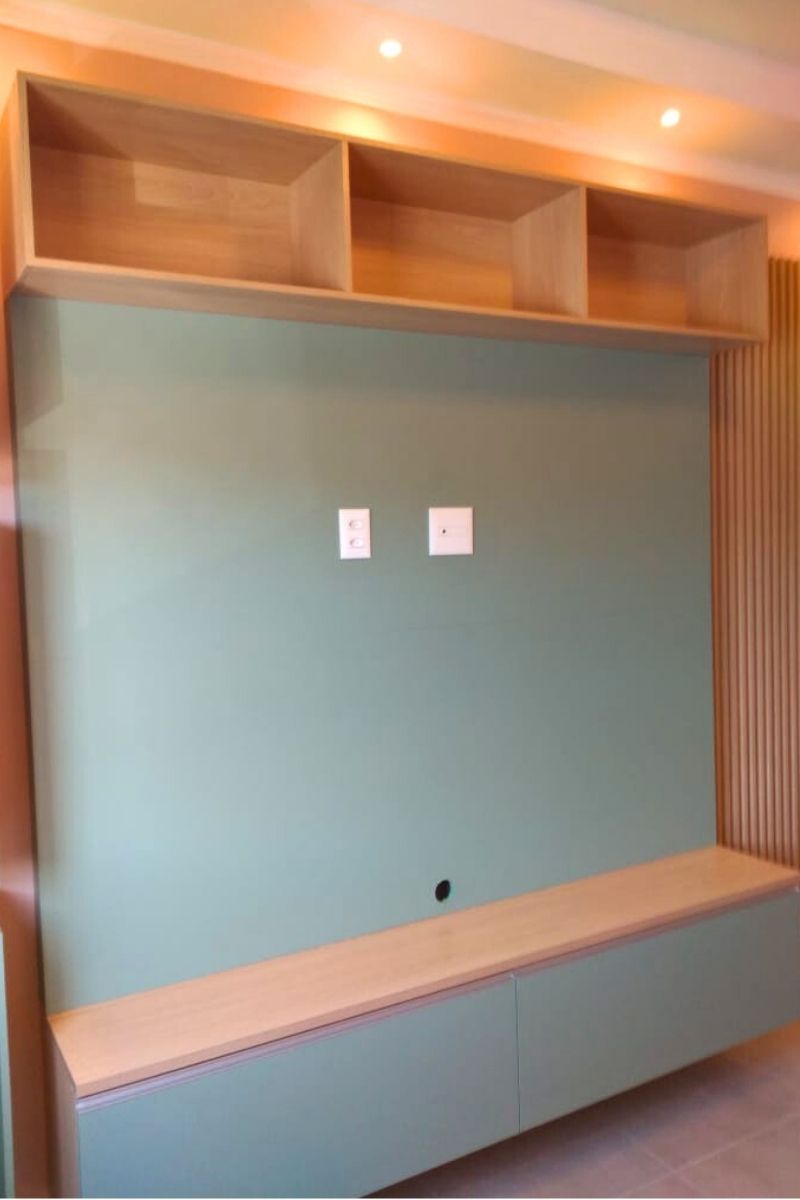 Painel para TV sob medida em tom verde suave (menta) com detalhe lateral decorativo em madeira ripada.
