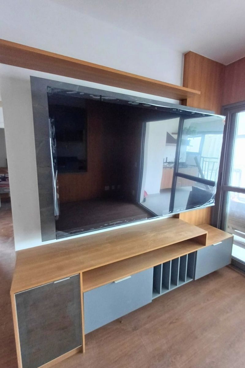 Projeto de sala de TV com painel escuro e rack de madeira suspenso, instalado próximo à porta da sacada.