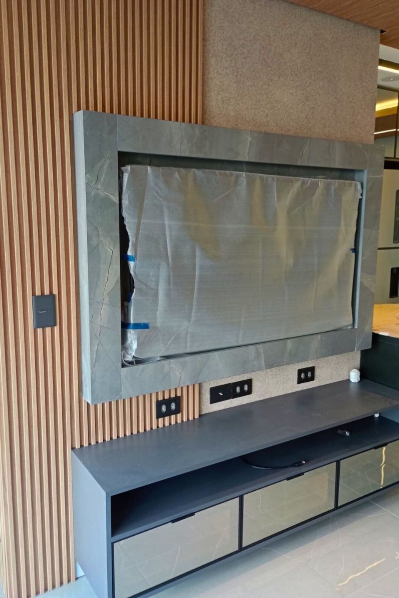 Detalhe de marcenaria: combinação de painel ripado de madeira com estrutura central marmorizada para a TV.