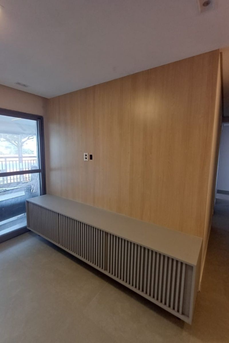 Revestimento de parede completo em madeira clara com móvel baixo ripado (banco ou rack), ideal para salas minimalistas.