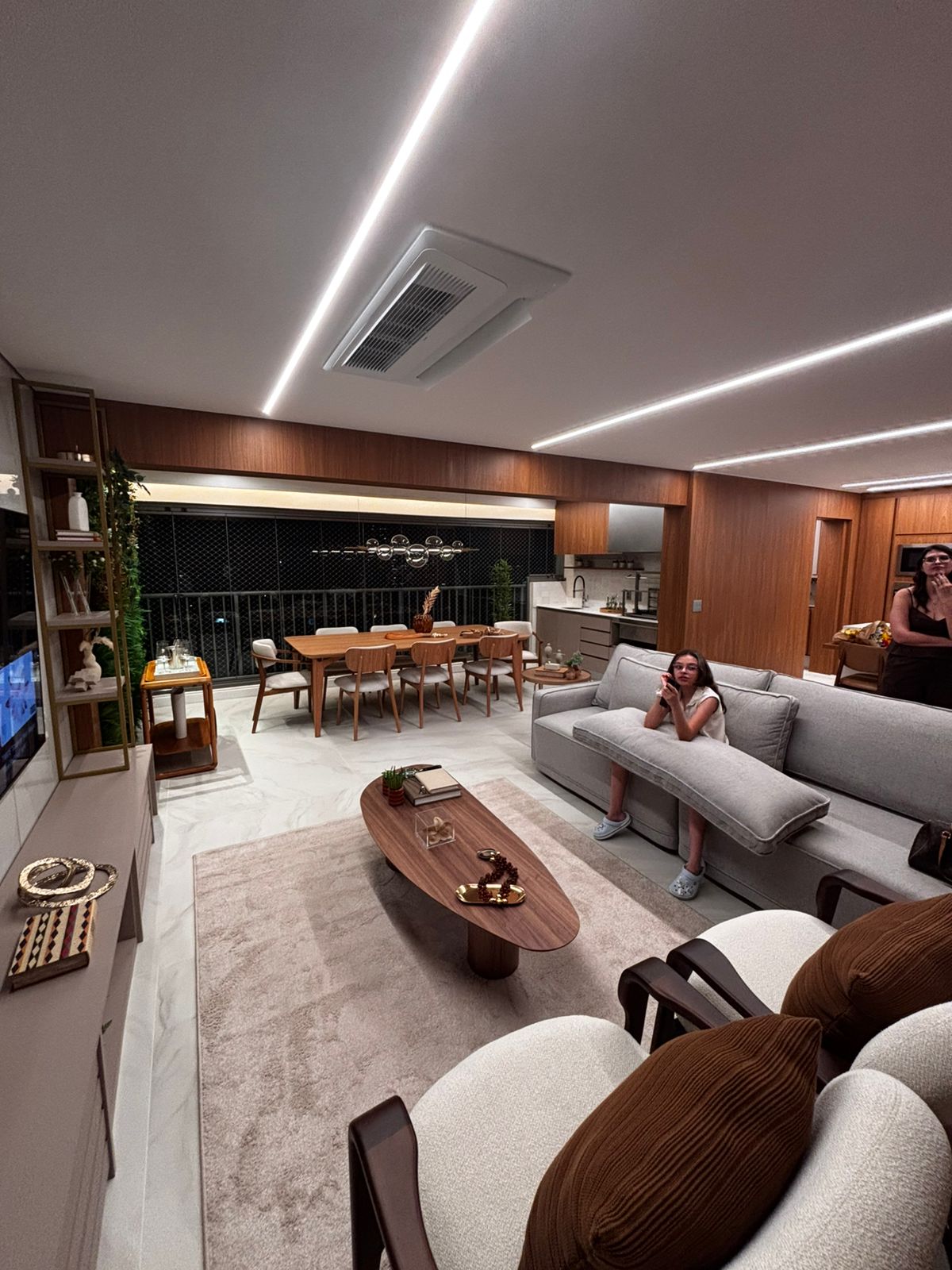 Sala de estar ampla com home theater planejado, rack baixo alongado e integração com a varanda do apartamento.